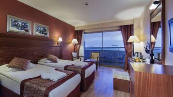 A hotel room with two beds, a desk, a chair, a TV, and a balcony with a view.