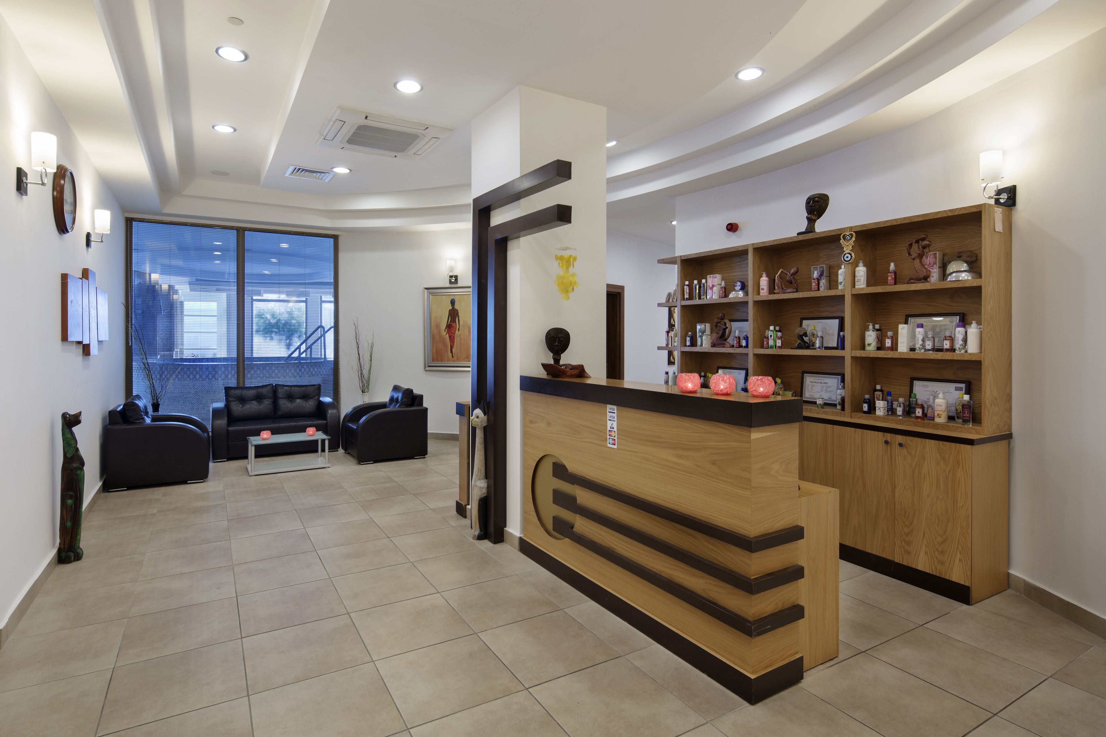 Un espace d’accueil moderne, doté d’un comptoir de réception en bois, d’un coin salon avec des canapés et d’une grande fenêtre offrant une vue sur l’extérieur.