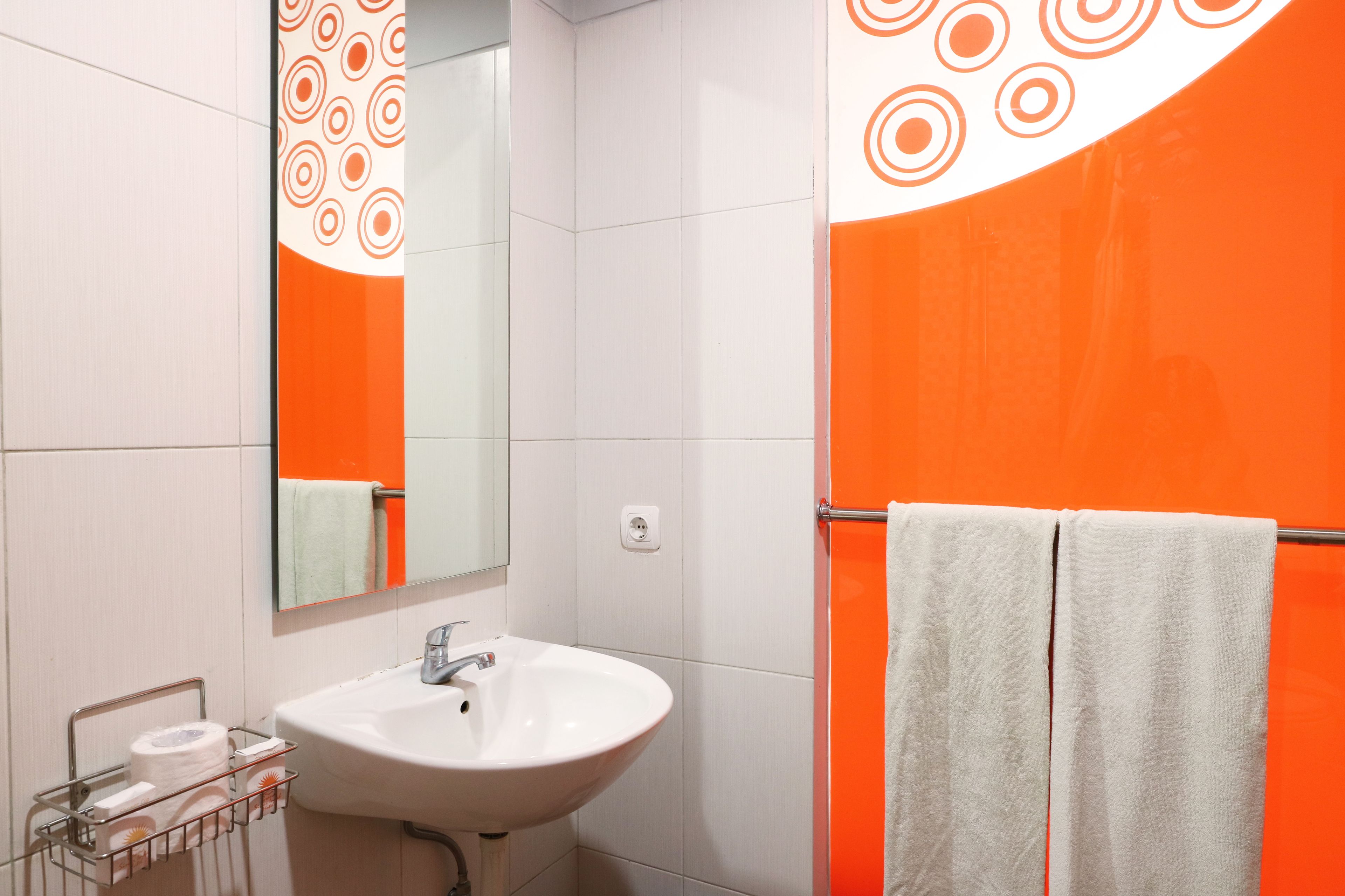 A bathroom with a white sink, a mirror, and an orange accent wall.