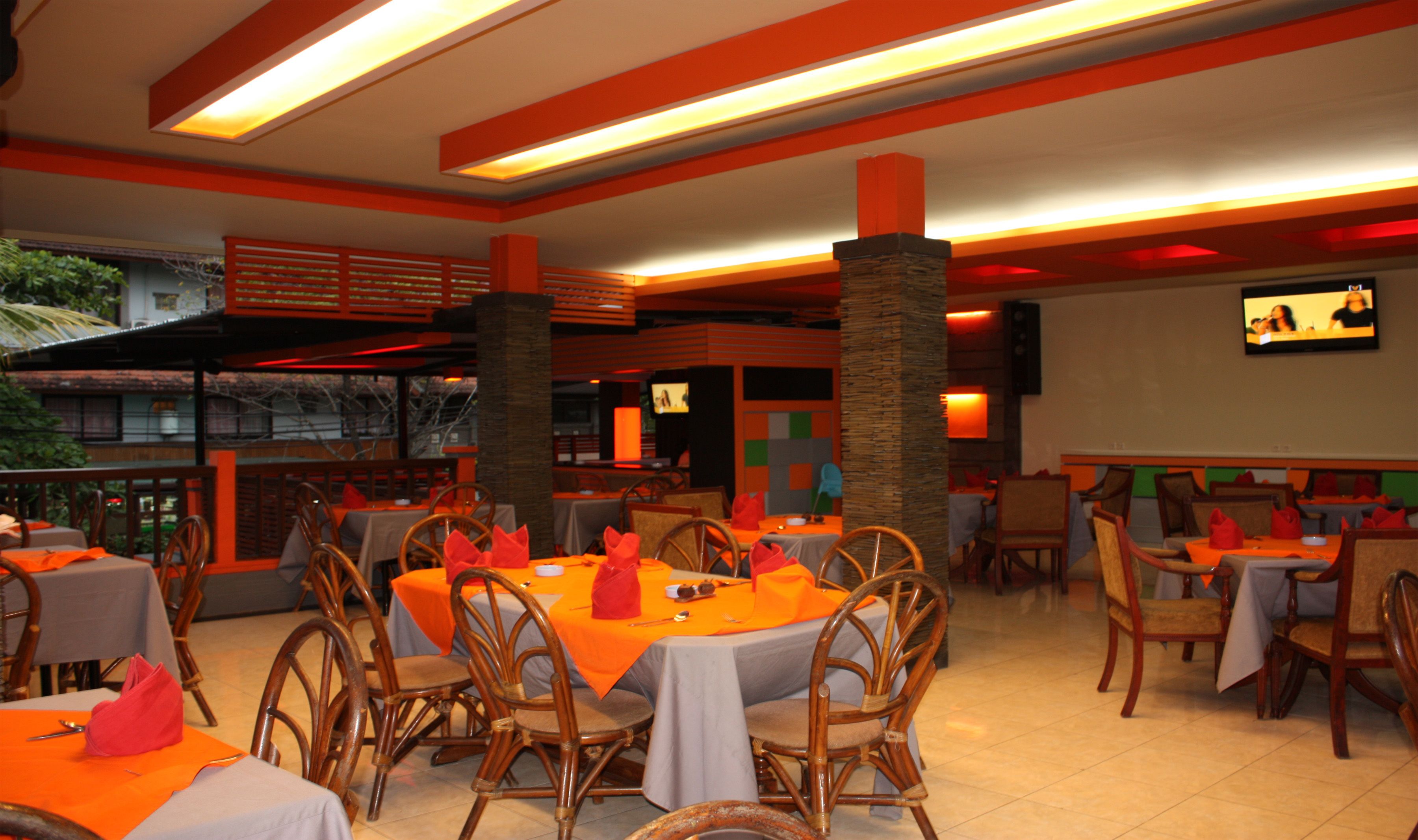 A restaurant with round tables, orange tablecloths, and wooden chairs.