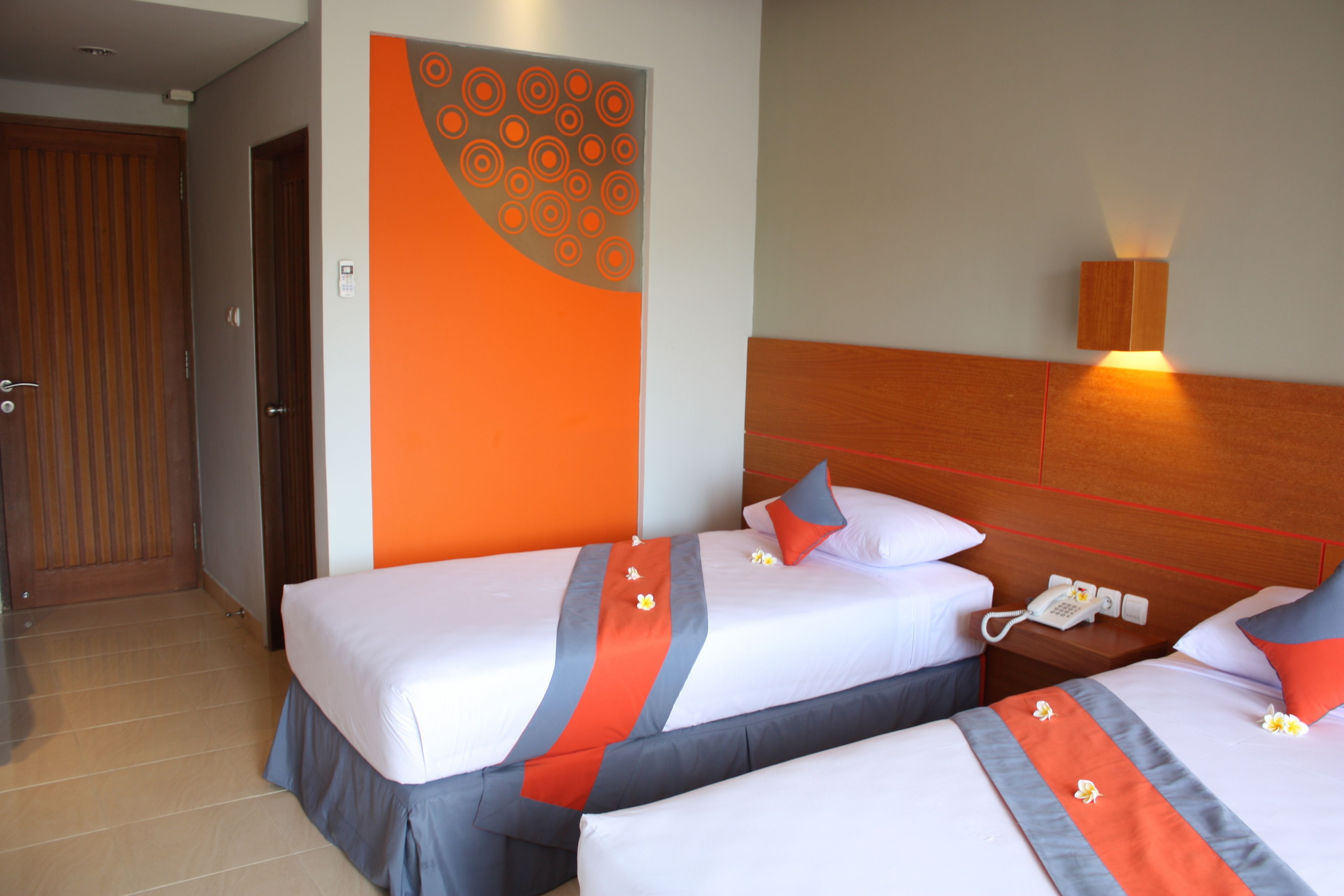 A hotel room with two beds, a wooden headboard, a wall-mounted phone, and a door.
