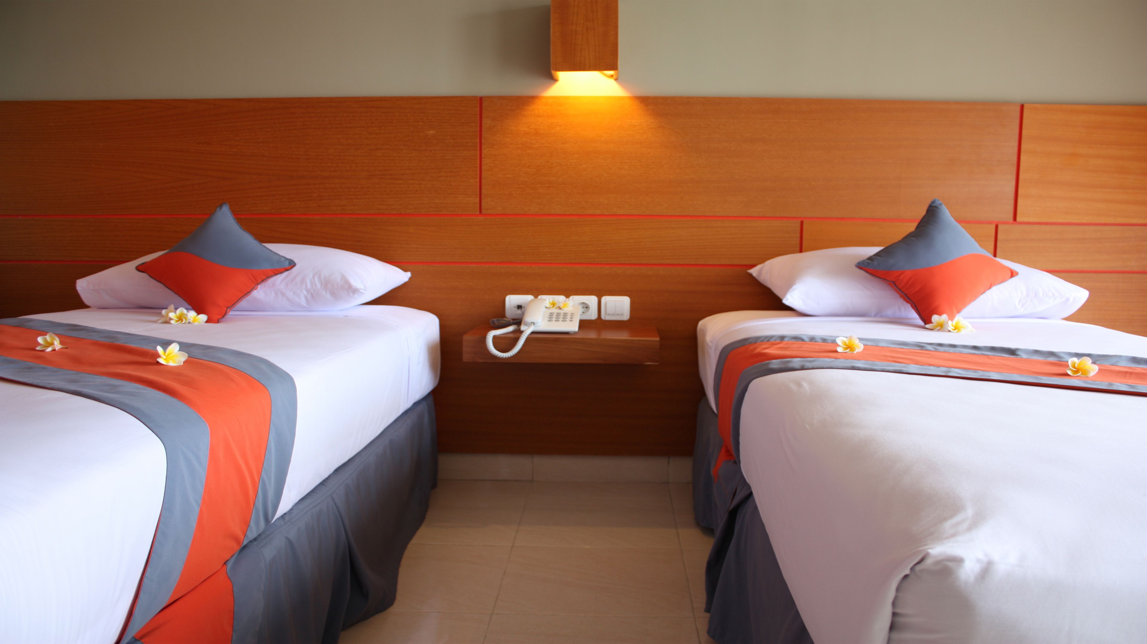 Two adjacent hotel beds with matching headboards, a bedside telephone, and a wall-mounted light fixture.