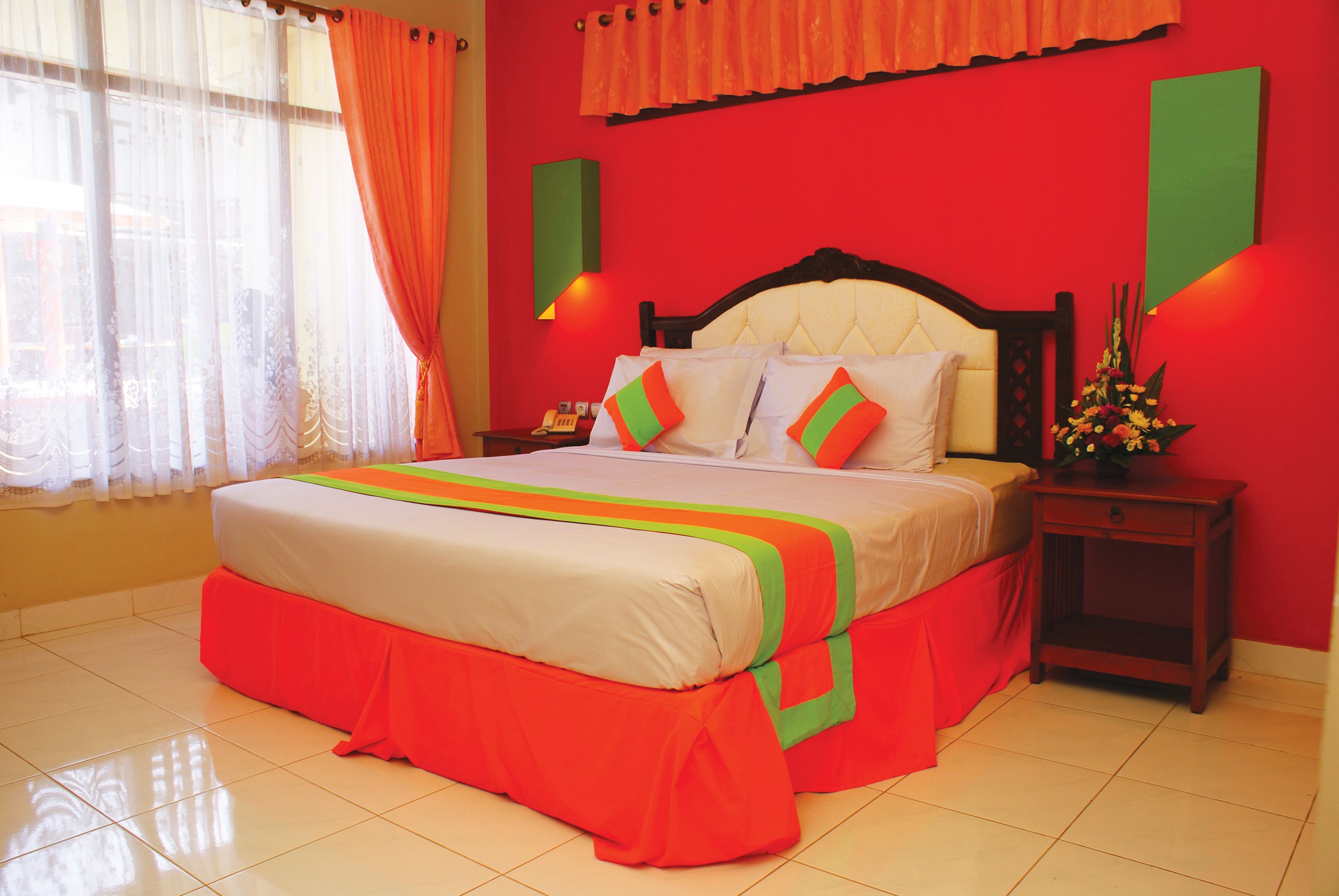 A hotel room with a large bed, a nightstand, a vase of flowers, and a window with curtains.