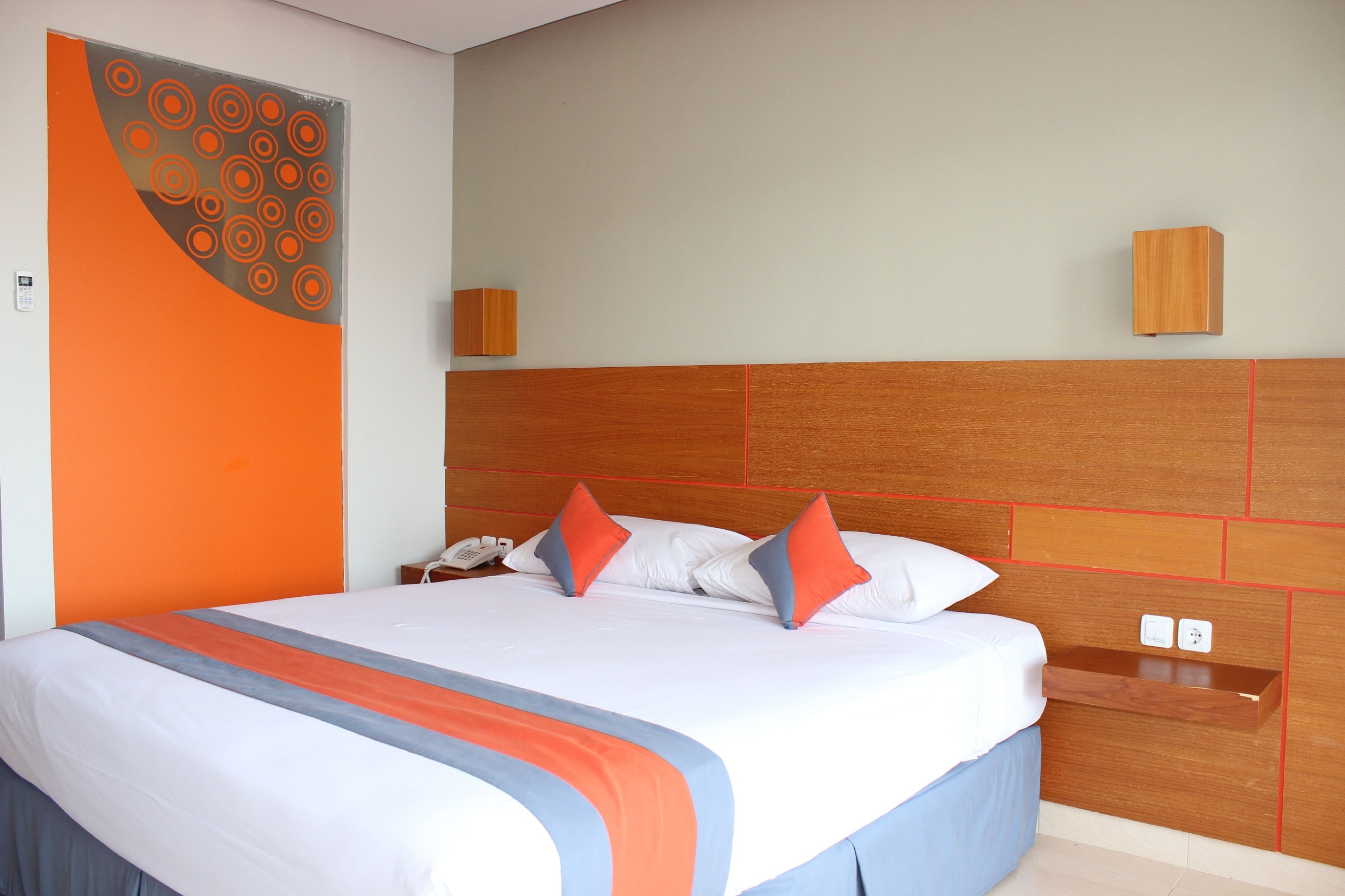 A hotel room with a large bed, a wooden headboard, a bedside table with a phone, and a wall-mounted light.