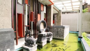 A koi pond with fish, a stone sculpture, and a traditional building with red and white accents. - Grand Sinar Indah Hotel (Legian)