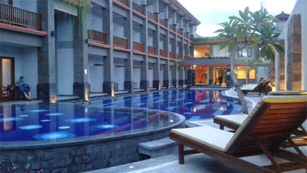 A swimming pool with lounge chairs, a stone wall, and a building with multiple balconies. - Grand Sinar Indah Hotel (Legian)