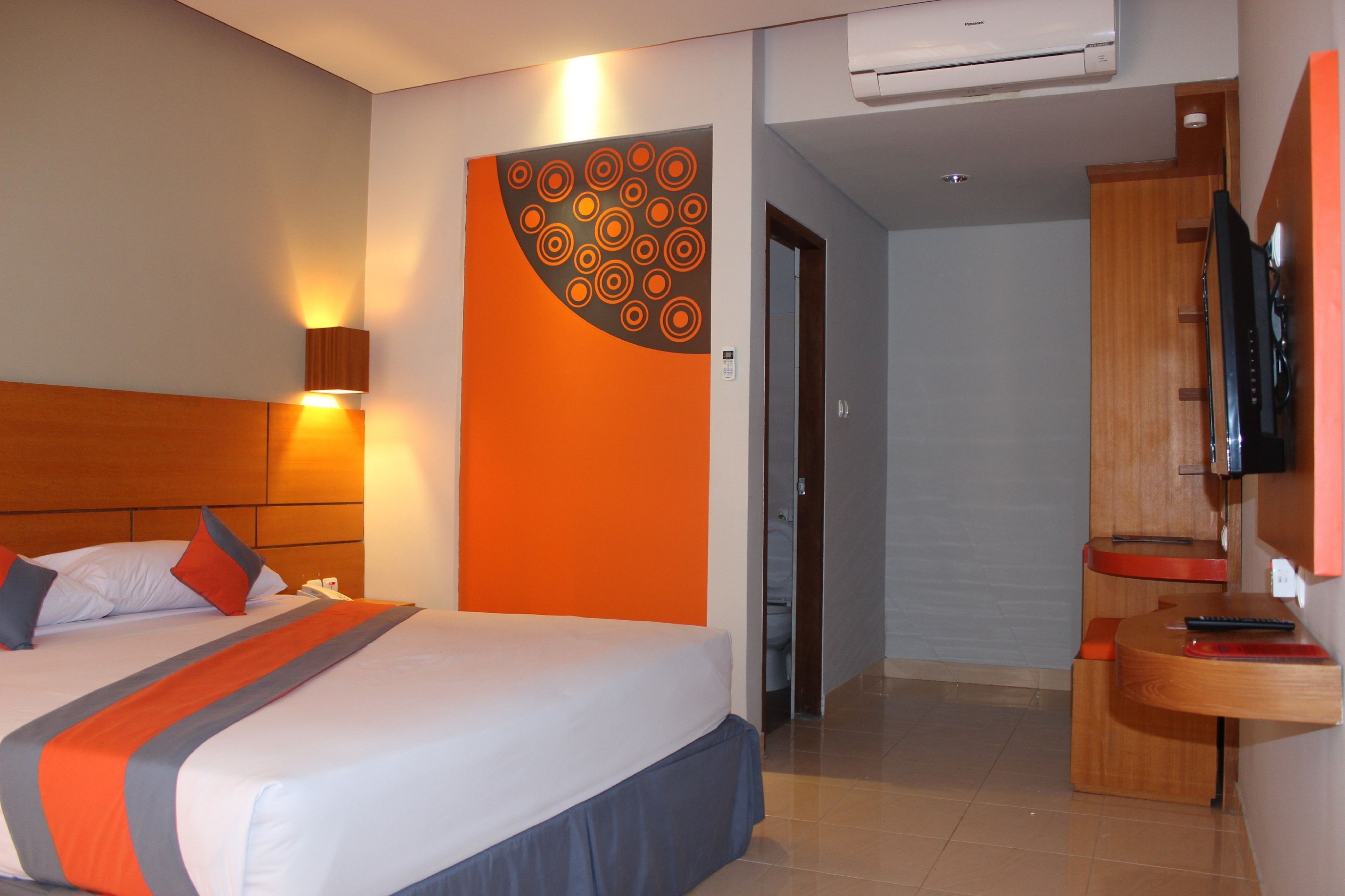 A hotel room with a bed, a TV, a desk, and a bathroom visible through an open door.