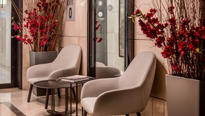 Un vestíbulo con dos sillones color beige, una mesita redonda y una planta en maceta con flores rojas.