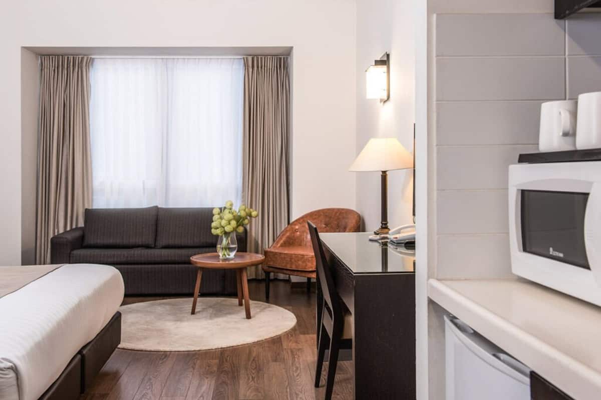 Une chambre d’hôtel comprenant un lit, un canapé, une petite table ronde avec une lampe, une télévision et un coin cuisine.