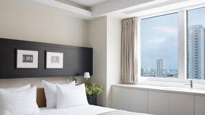 Una habitación de hotel moderna con una cama grande, vistas a la ciudad, obras de arte enmarcadas en la pared y una ventana con cortinas.
