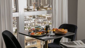 Una mesa de desayuno con vista a la ciudad, un periódico y un bol de fruta.