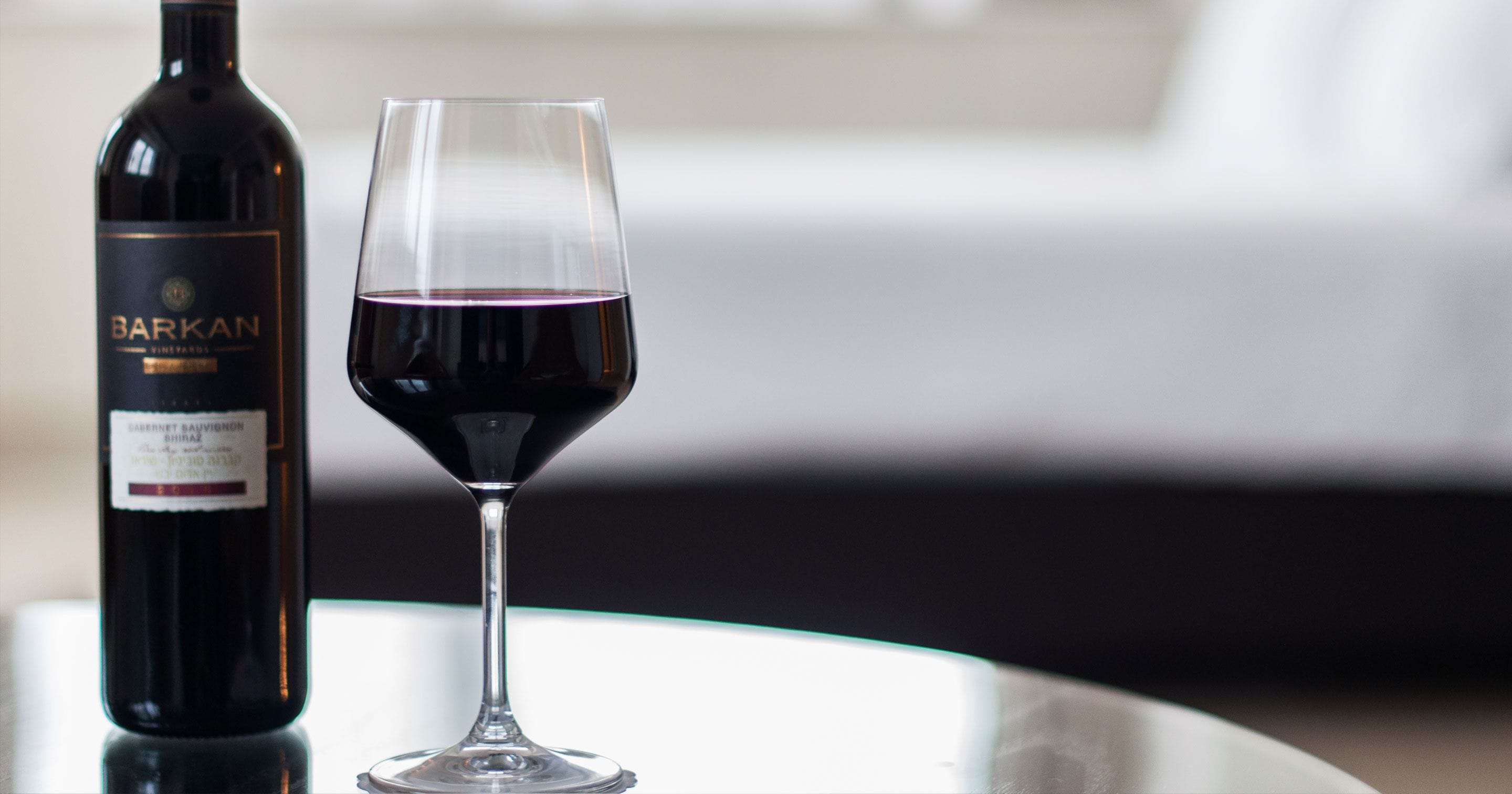 A bottle of wine and a glass of red wine on a table.