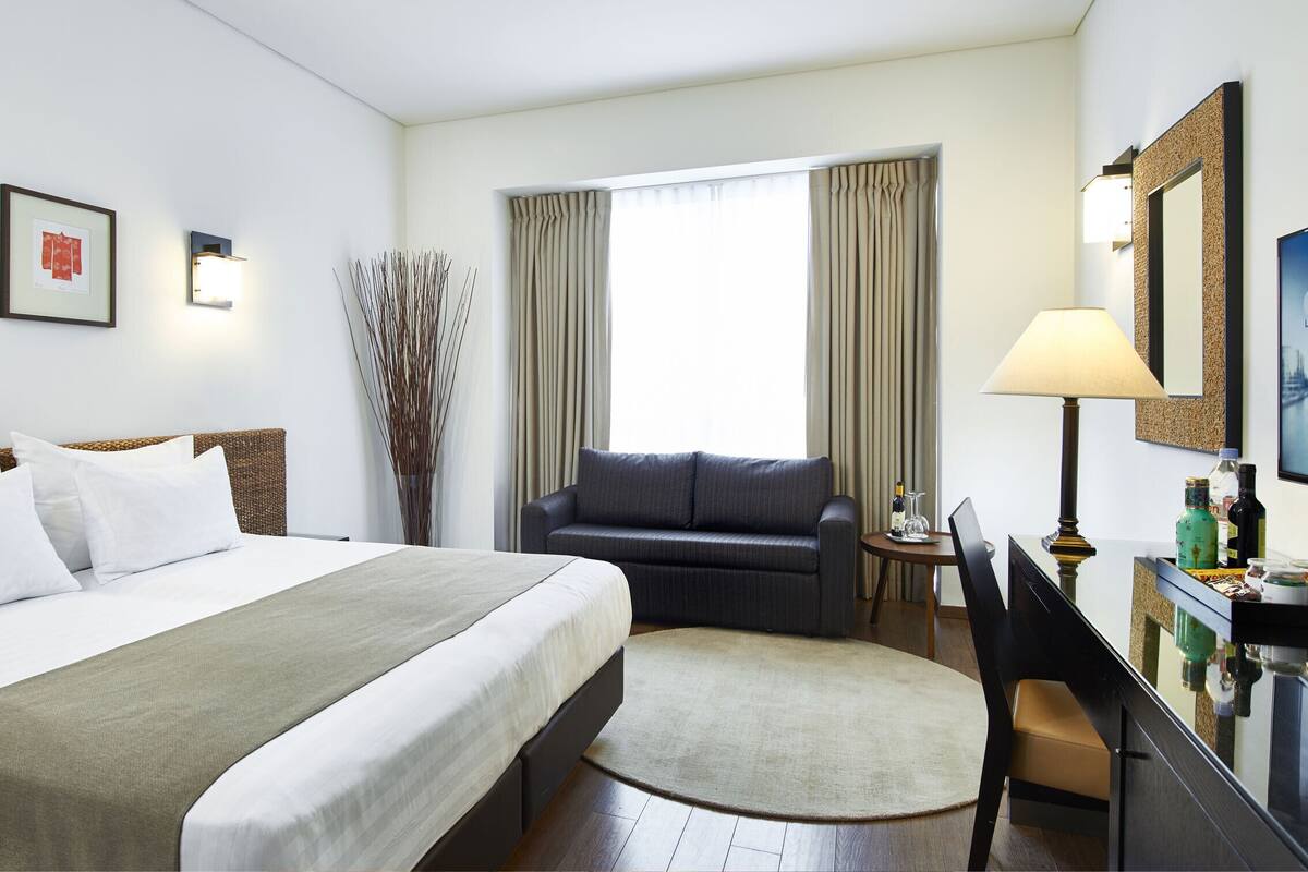 A hotel room with a bed, a desk, a chair, a lamp, and a TV.