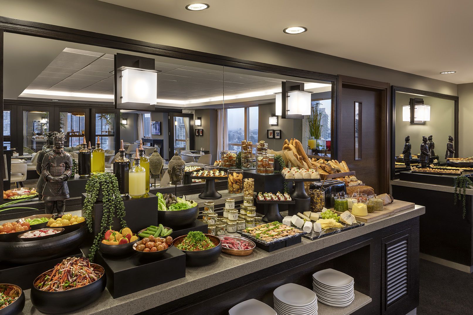 A buffet with various food items and condiments, including fruits, vegetables, cheeses, and meats, arranged on a counter with a mirror reflecting the room.