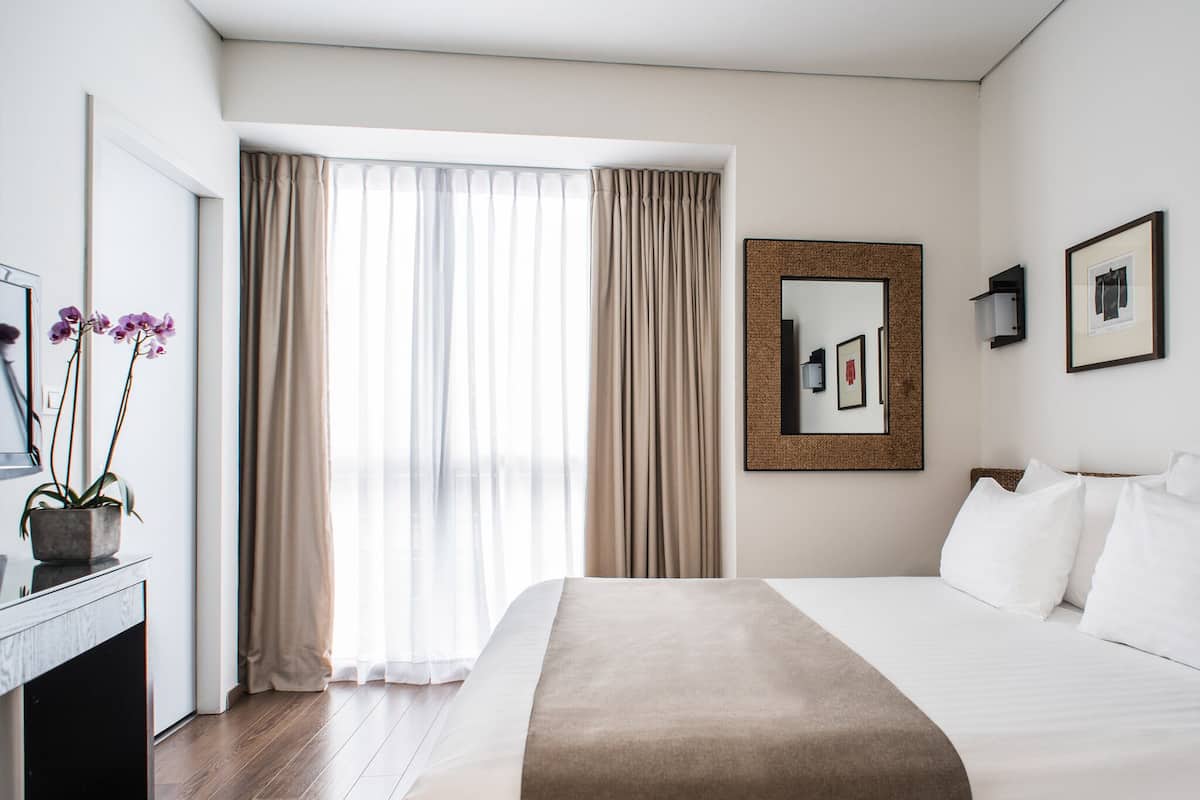 A hotel room with a large bed, a desk with a computer, a mirror, and a window with curtains.