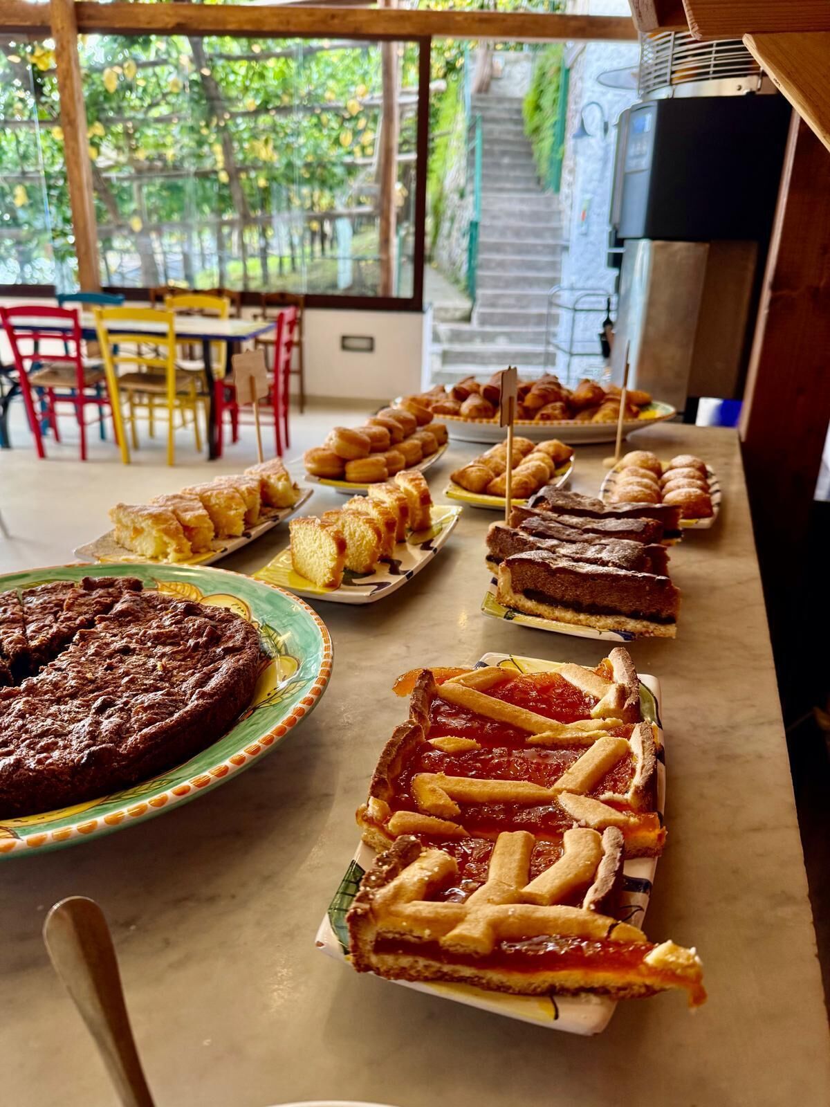 Une table de buffet proposant diverses pâtisseries, notamment des tartes et des viennoiseries, dans une pièce d’où l’on peut admirer la verdure environnante.