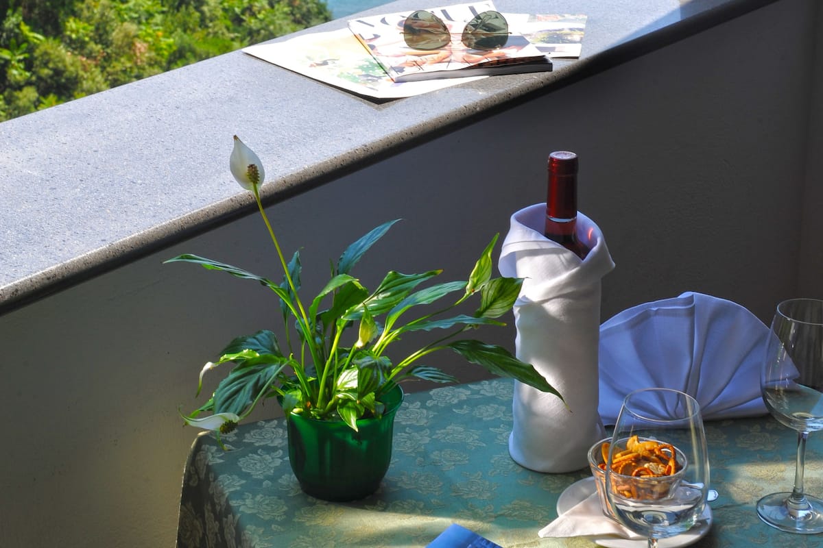 Un balcon avec vue sur l’océan, une table avec un livre, une bouteille de vin et un verre.