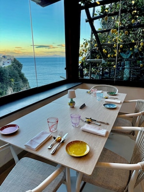 A dining table set with plates, cutlery, and glasses, overlooking a coastal view with a lemon tree. - Hotel La Pergola (Amalfi)