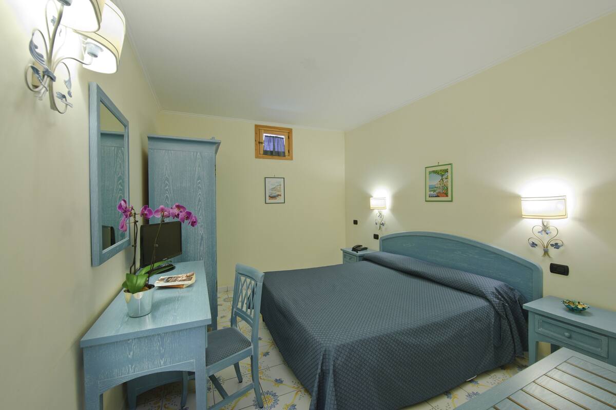 Une chambre à coucher comprenant un lit, un bureau avec une chaise, un miroir et deux tables de chevet avec des lampes.
