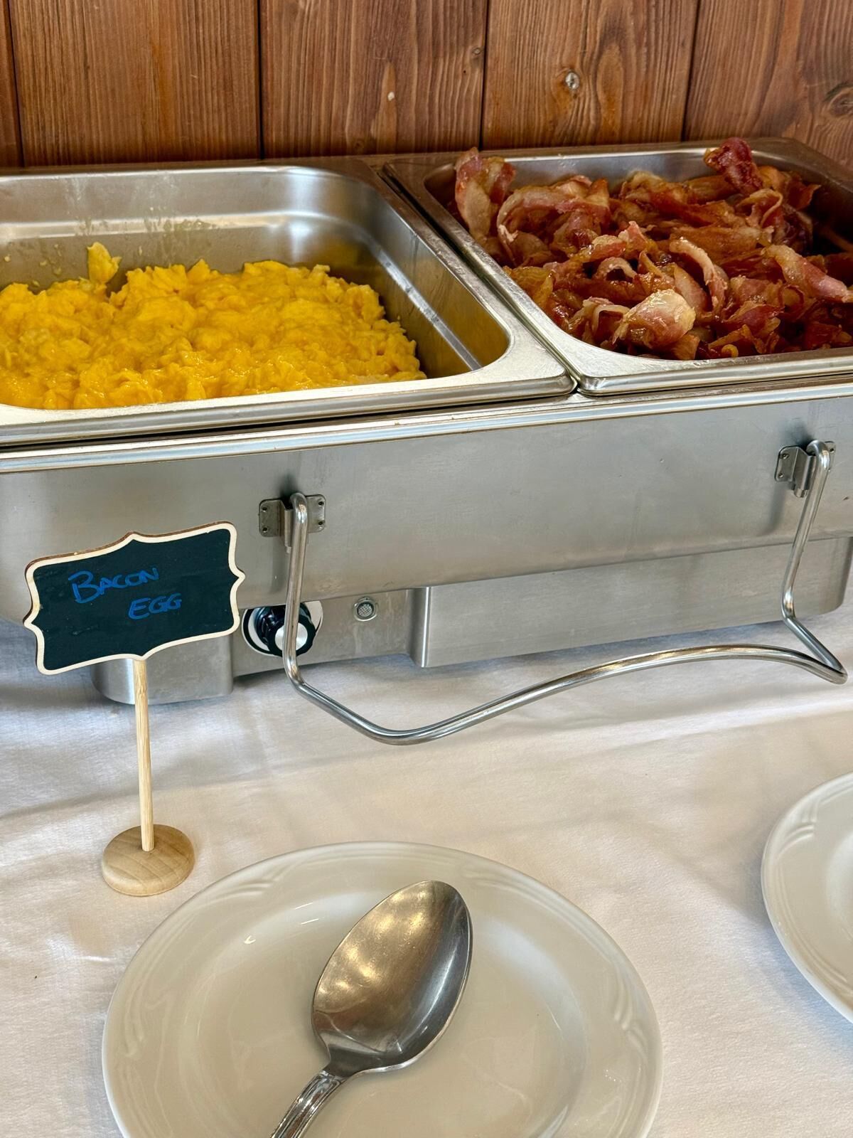 A buffet with labeled containers for bacon and egg, and a sign indicating the location.