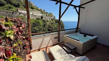 En balkon med jacuzzi, liggestole og udsigt til en bakke.