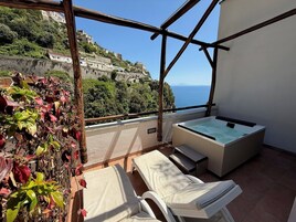Un balcón con hidromasaje, sillones de descanso y vistas a una colina.