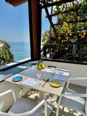 Mesa para dos con vista al mar, una pérgola de madera con limones y un paisaje costero.