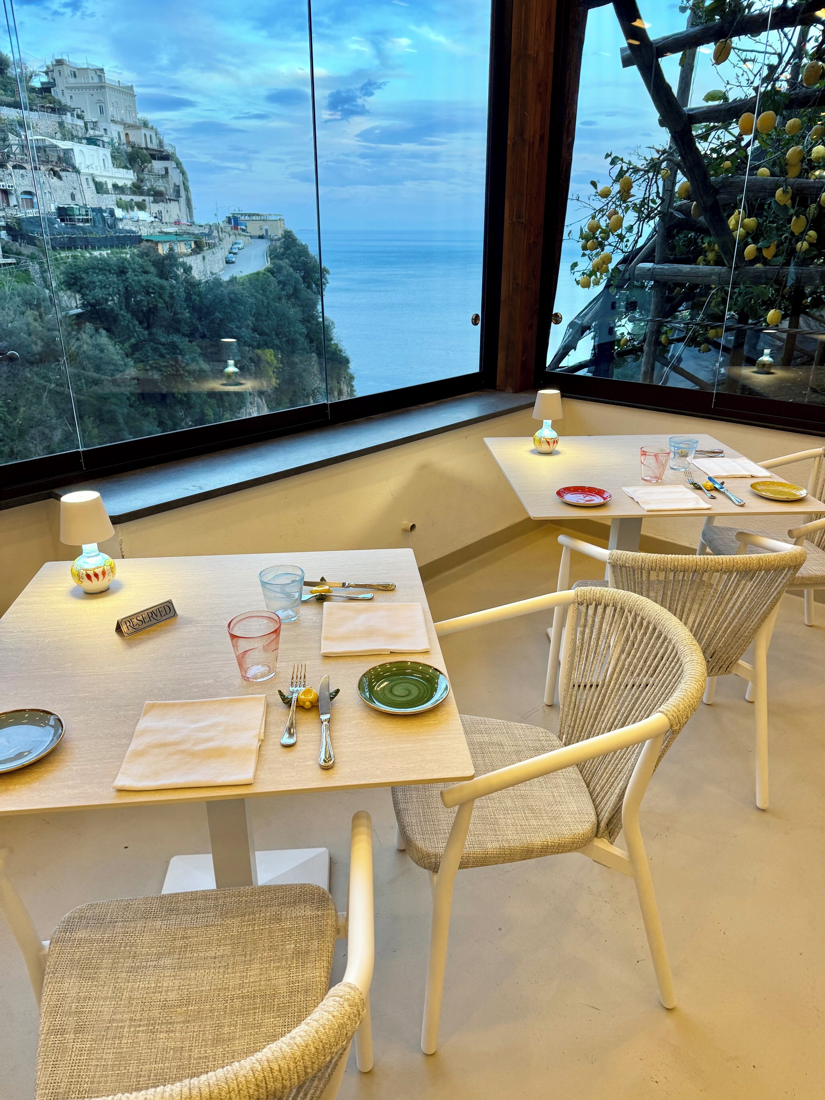 Un comedor con mesas y sillas, vista a un pueblo costero y un limonero.