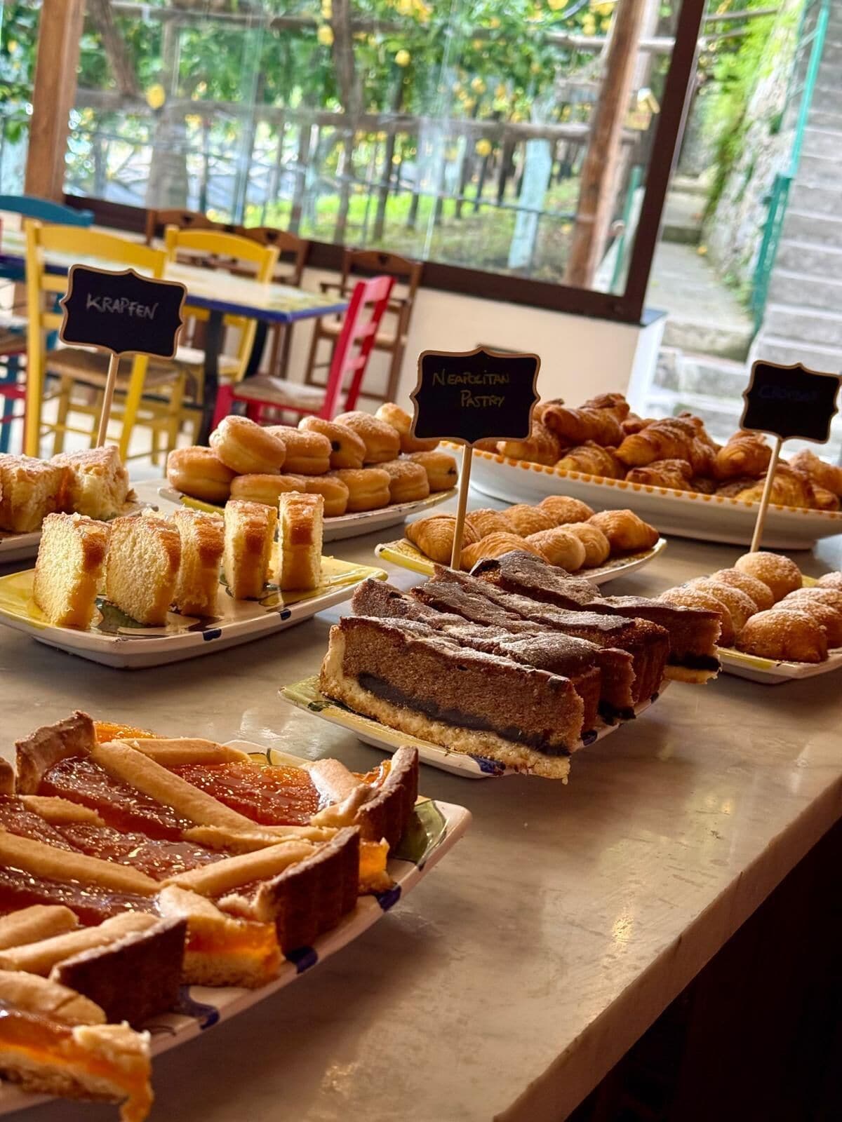 Eine Auswahl an Gebäck und Desserts präsentiert auf einer Theke, mit Schildern, die die verschiedenen Sorten bezeichnen.