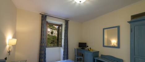 A bedroom with a bed, a desk, a chair, a wardrobe, and a window with curtains.