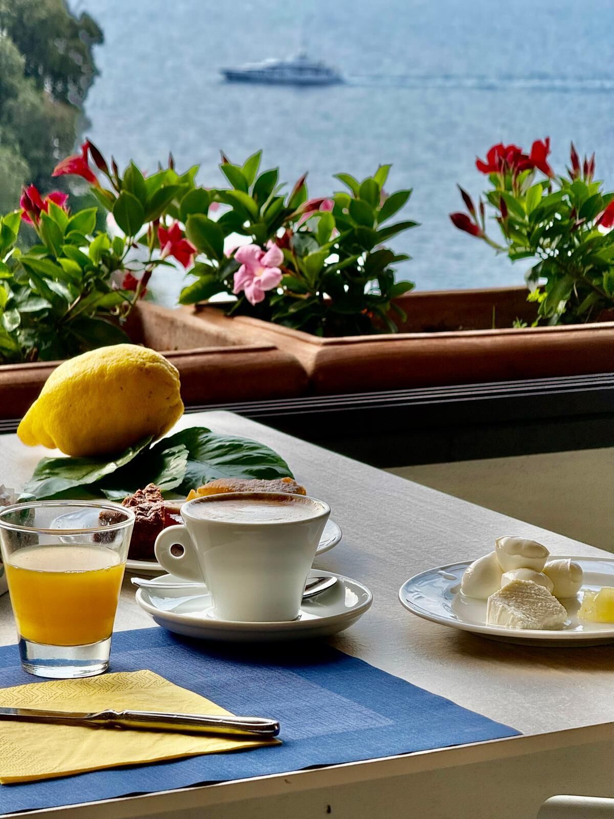 Una mesa con alimentos para el desayuno, un vaso de jugo de naranja y vista al mar.