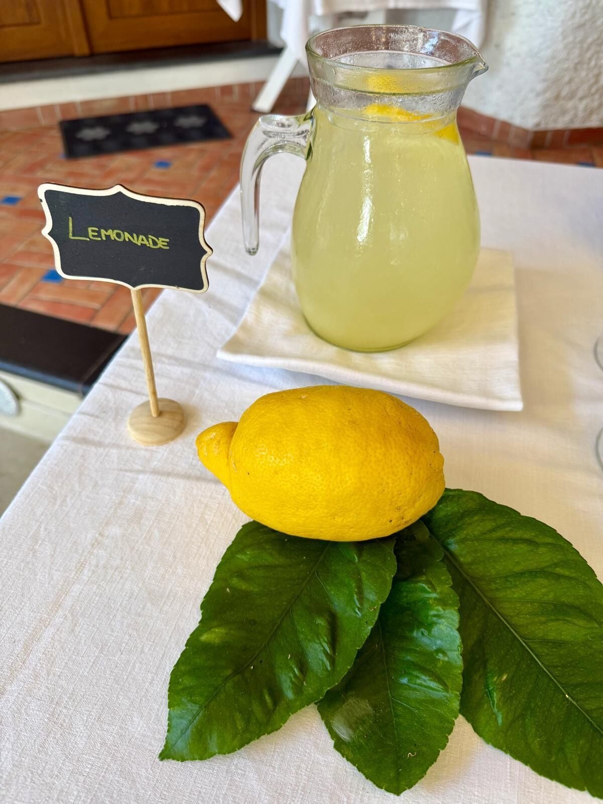 A pitcher of lemonade with a lemon and leaves on a table.
