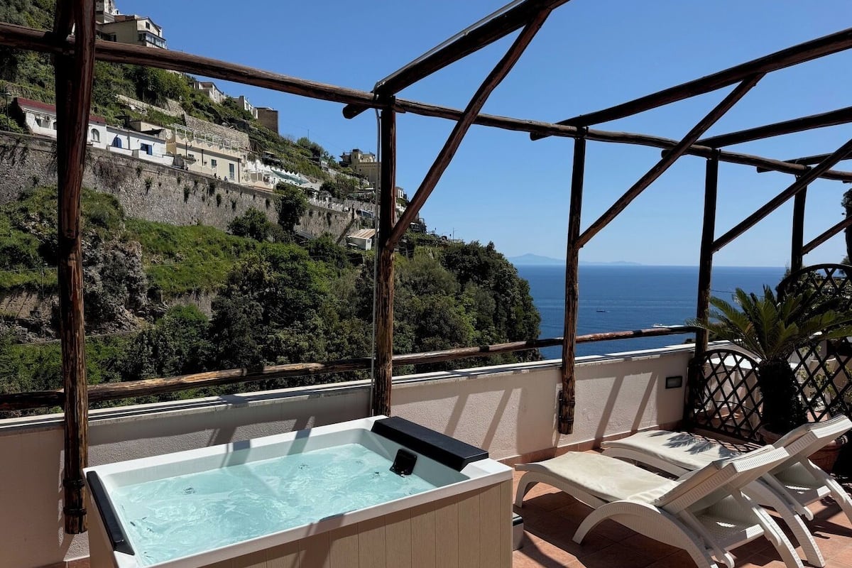 Un bain à remous, des chaises longues et une vue sur la mer et les bâtiments situés sur la colline.