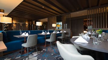 A modern restaurant with blue seating, white chairs, and a carpeted floor.