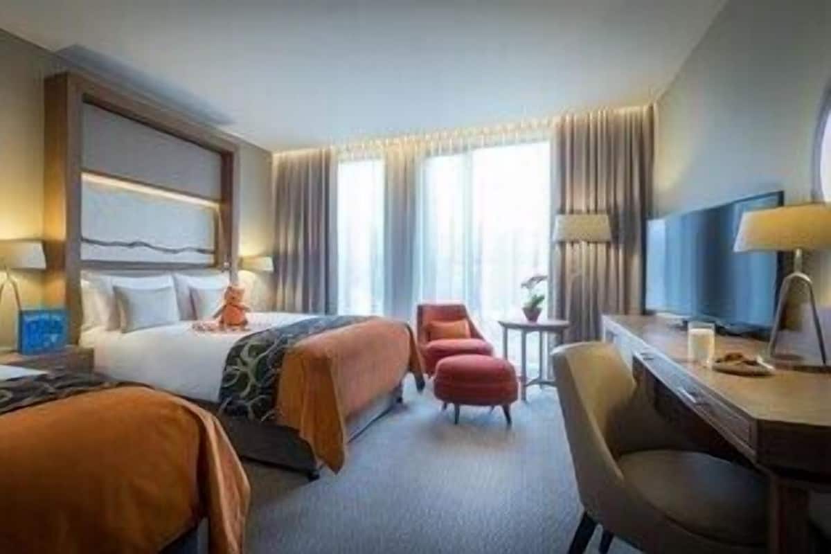 A hotel room with a bed, two chairs, a desk, and a lamp.