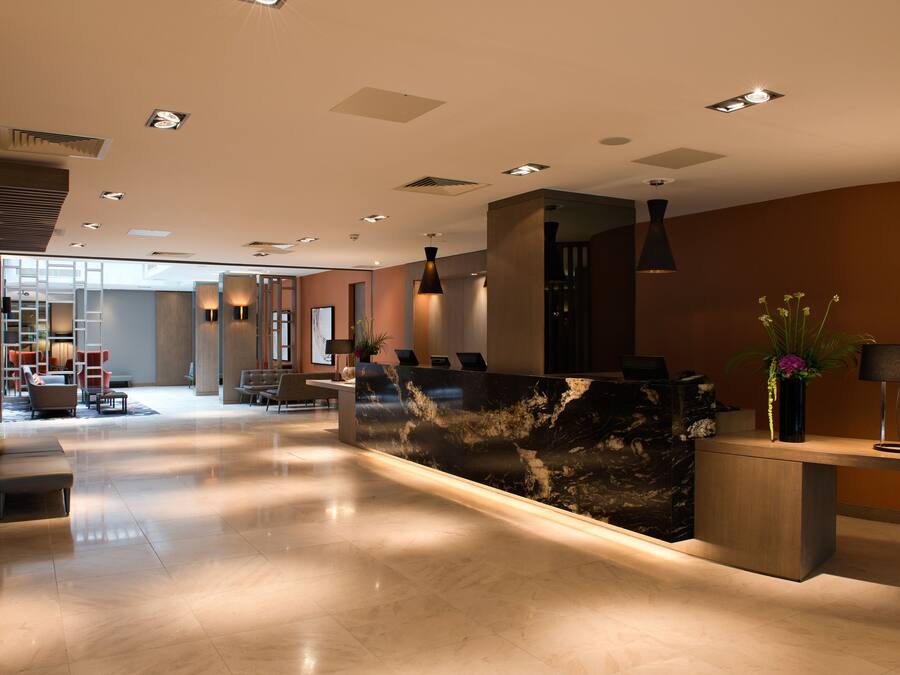 A modern hotel lobby with a marble reception desk, seating area, and a view into the dining space.