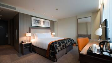 A hotel room with a bed, bedside table, lamp, chair, desk, and a large mirror.