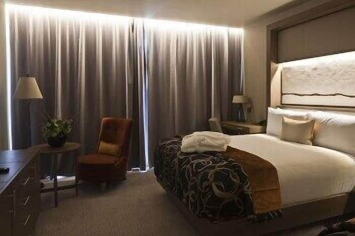 A hotel room with a bed, a chair, a desk, and a lamp.