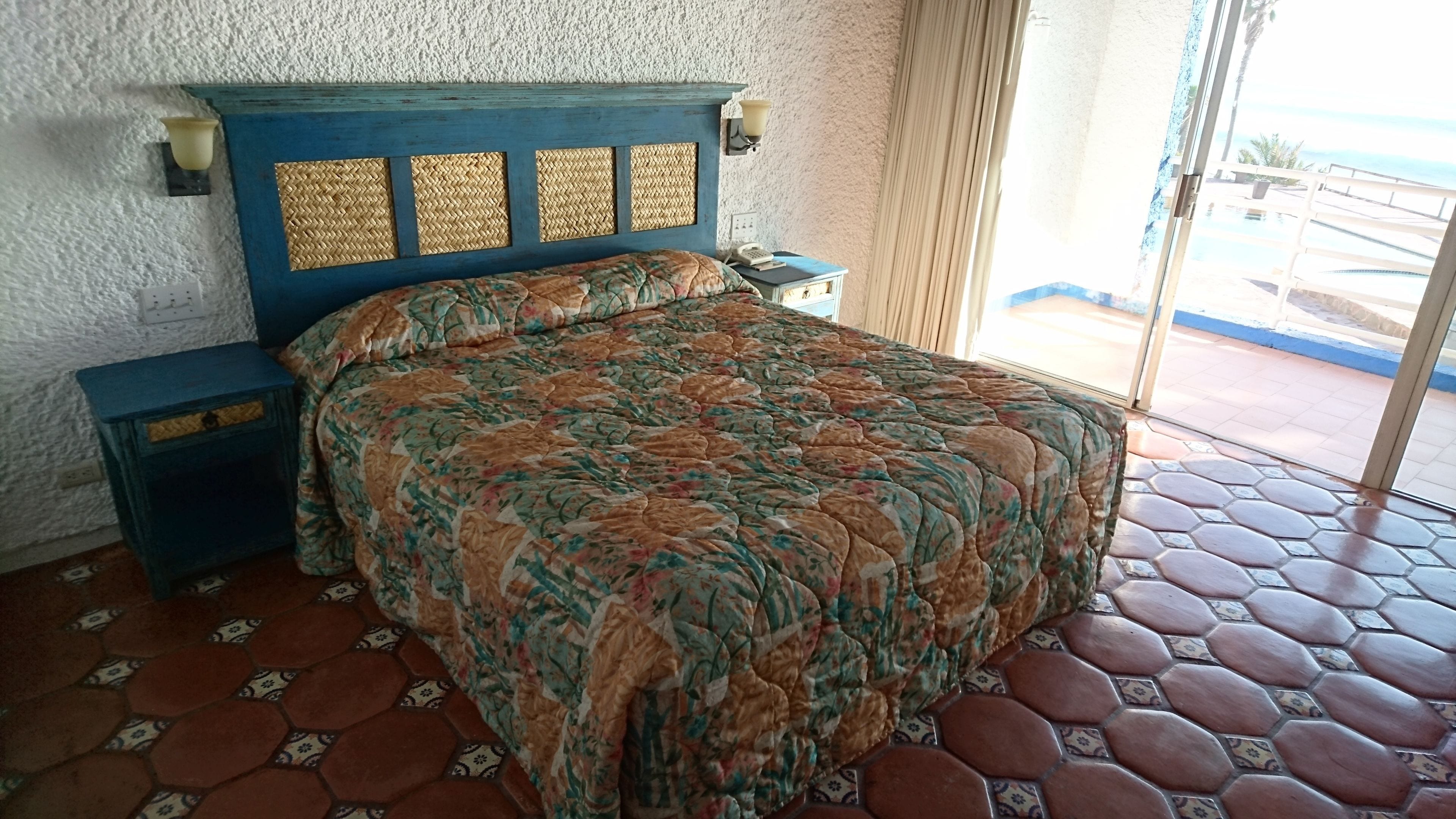 A room with a bed, a nightstand, a lamp, and a view of the outside.