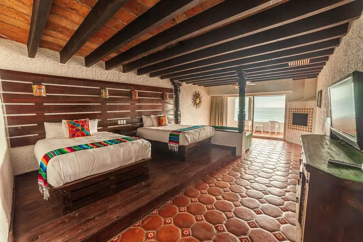 A room with two beds, a wooden ceiling, and a view of the sea.