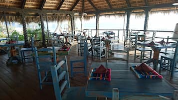 A covered outdoor dining area with wooden tables and chairs, some with red napkins.