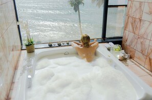A bathtub with a view of the ocean, a potted plant, and toiletries on the side.