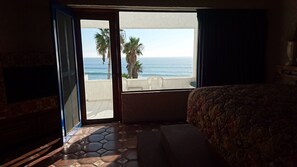 A hotel room with a bed, a view of the ocean, and a balcony with chairs.