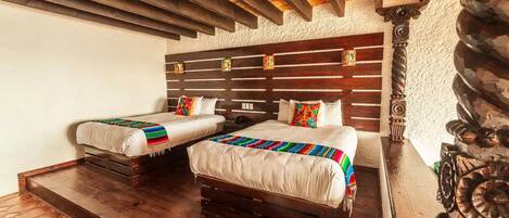 A room with two beds, wooden flooring, a rustic ceiling, and a decorative column.