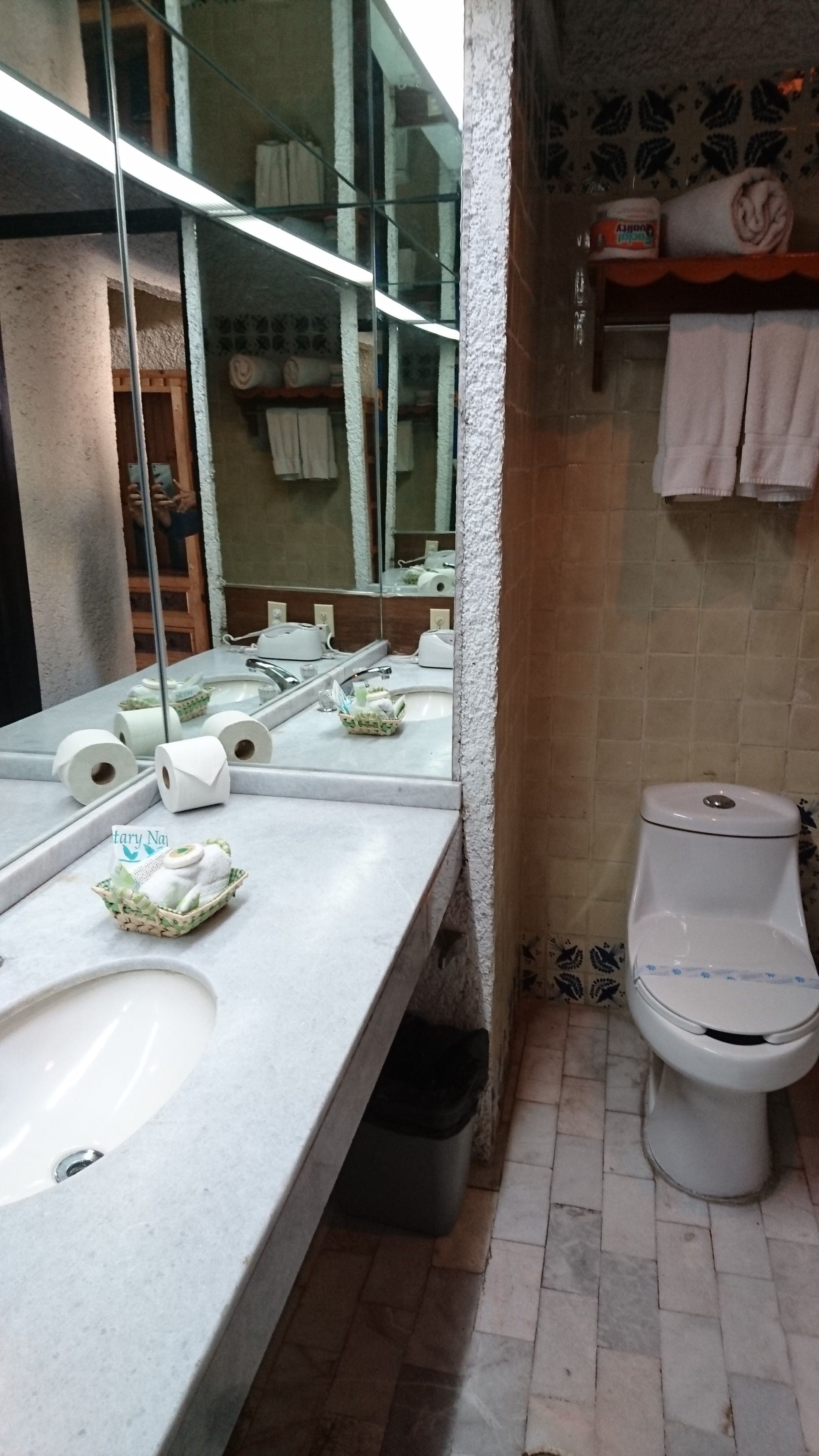 Un baño con lavamanos, espejo, inodoro y repisas con toallas.