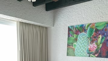 Un salon comprenant un canapé d’angle, une table ronde, un ventilateur de plafond et un grand tableau représentant un cactus accroché au mur.