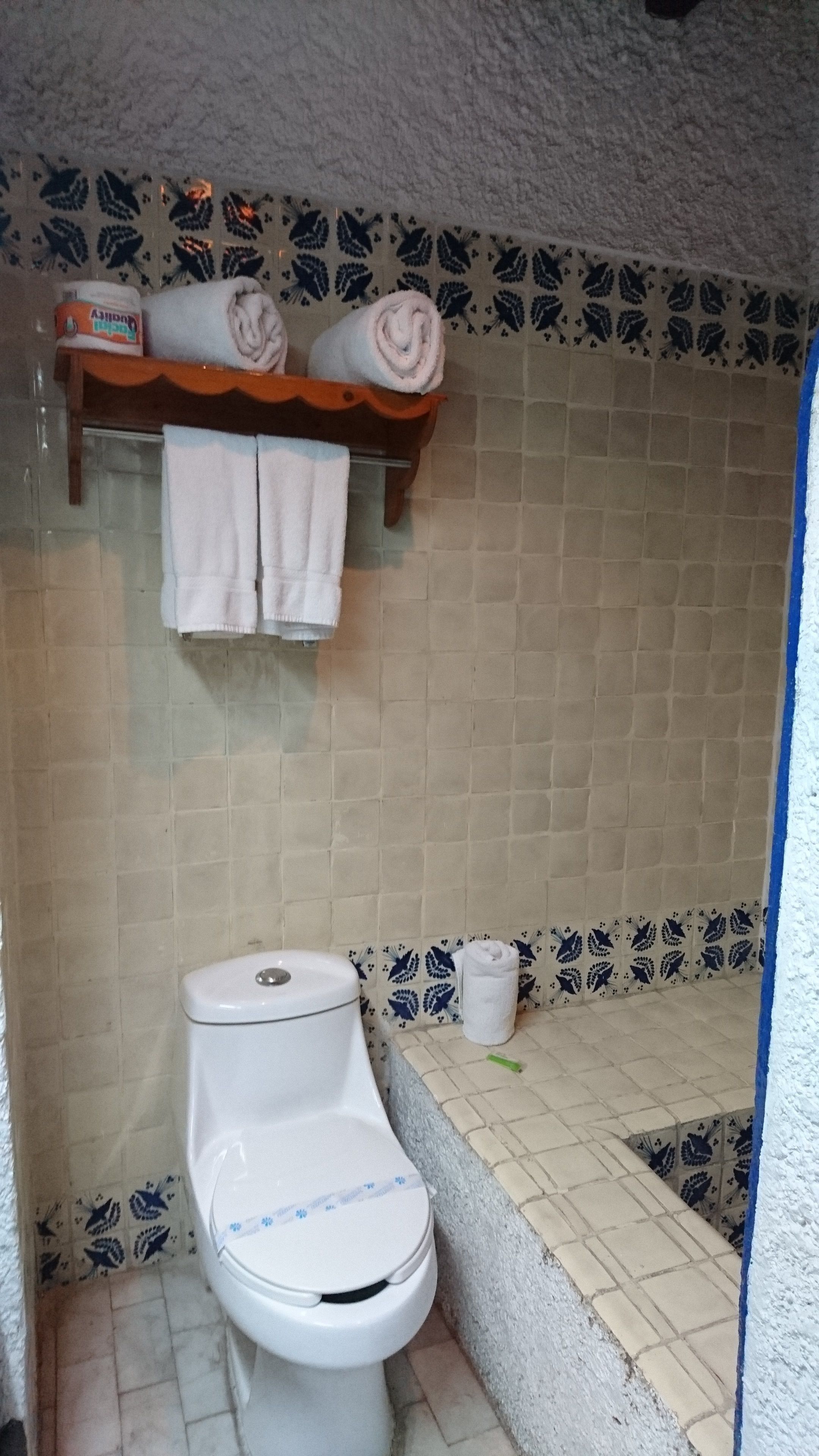 A bathroom with a toilet, a towel rack with towels, and a shelf with toiletries.
