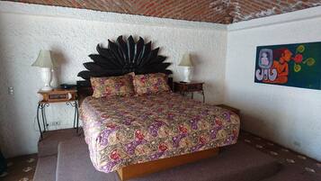 A bedroom with a large bed, two bedside tables, a decorative headboard, and a colorful painting on the wall.