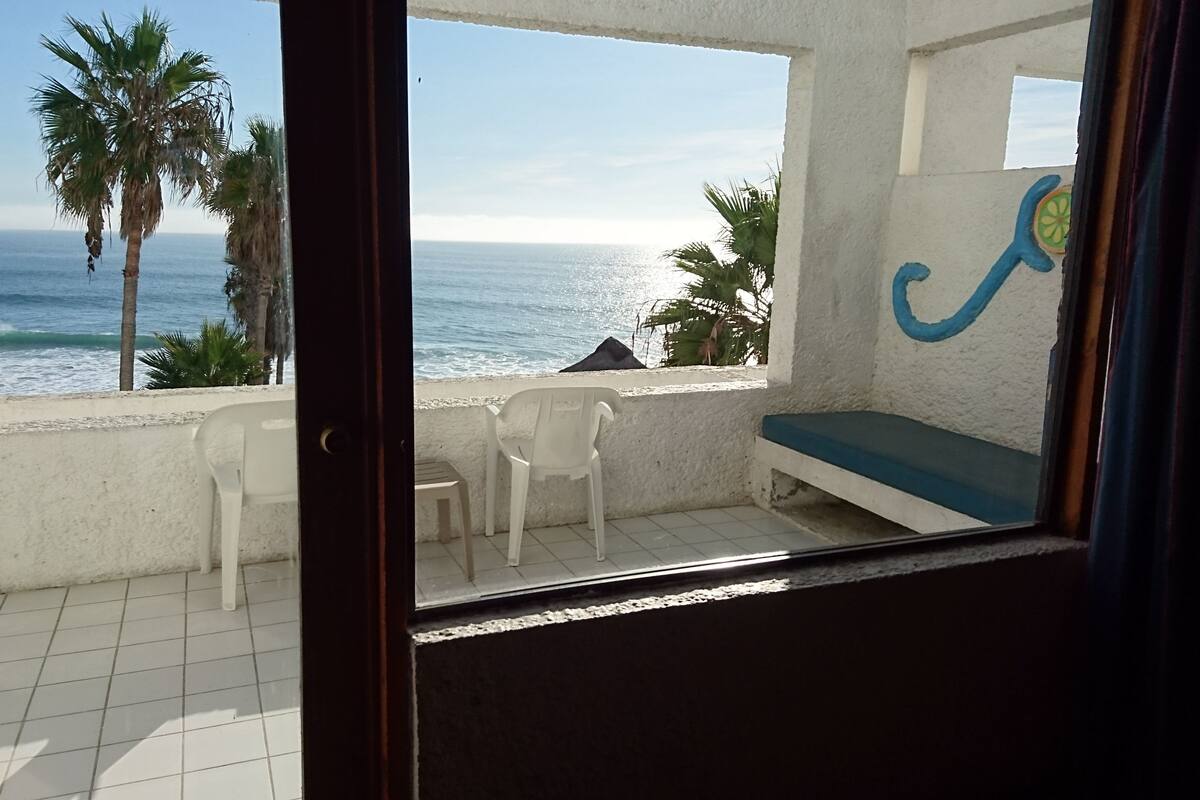 A balcony with a view of the ocean, a white wall with a blue design, and a white plastic chair.