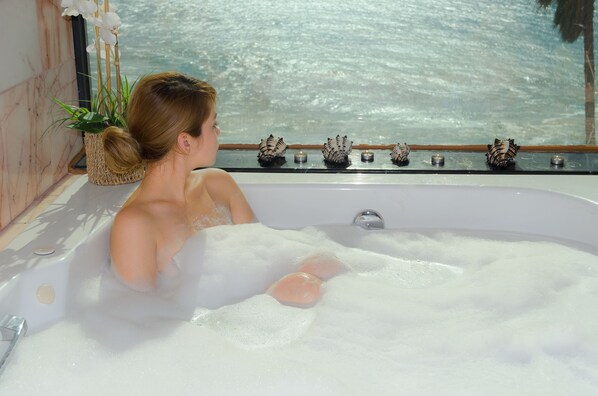 A bathtub filled with bubbles, a potted plant, and decorative shells.